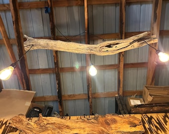 May include: Rustic wooden light fixture with three Edison-style bulbs hanging from a natural driftwood beam. The fixture is suspended from the ceiling with a chain, creating a warm, inviting ambiance. The wood has a natural, weathered appearance.