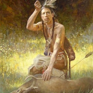 Op de afbeelding: Een indiaanse man in traditionele kleding zit met een hand op een hertenkarkas. Hij draagt een verenhoofdtooi en een kralenketting. De sc&egrave;ne speelt zich af in een bosclearing met zonlicht dat door de bomen valt.