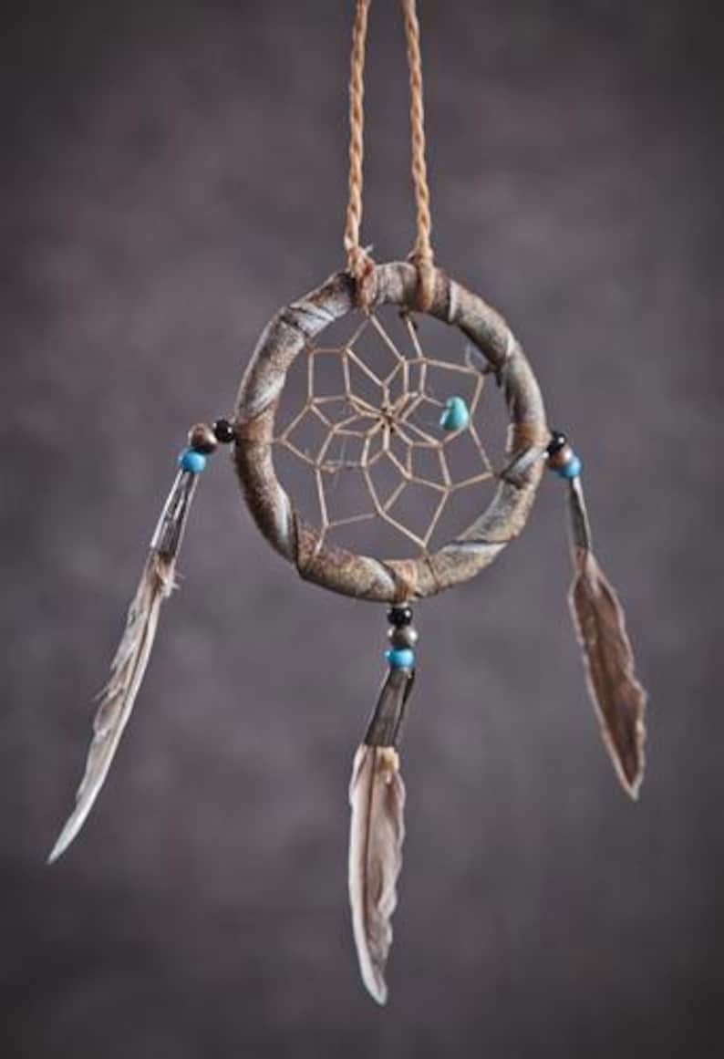 May include: A brown dream catcher with a white web and blue beads hanging from it. The dream catcher has three brown feathers attached to it.