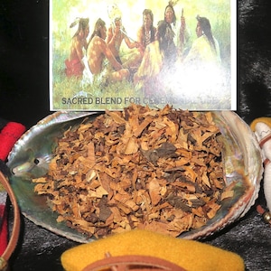 May include: A close-up of a seashell filled with dried herbs and wood chips. The shell is sitting on a brown and black striped blanket. A card with the text "Sacred Blend for Ceremony" is visible in the background.