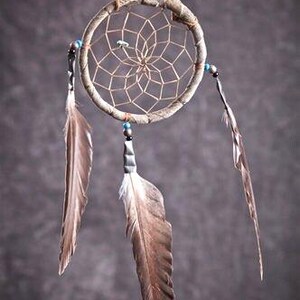 May include: A brown dream catcher with a woven web and feathers hanging from the bottom. The dream catcher is decorated with blue beads.