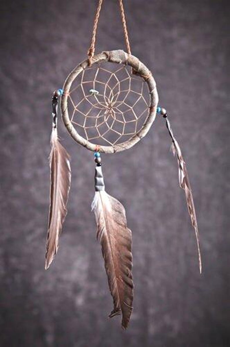 May include: A brown dream catcher with a woven web and feathers hanging from the bottom. The dream catcher is decorated with blue beads.
