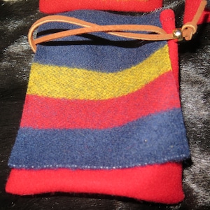 May include: A small, blue, red, and yellow striped pouch with a brown leather strap and a gold metal clasp. The pouch is made of a soft, fuzzy fabric.