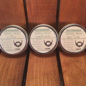 May include: Three round metal tins with labels for beard balm. The labels are white with black text and a green beard icon. The scents are Citrus, Lumberjack, and Bay Lime.