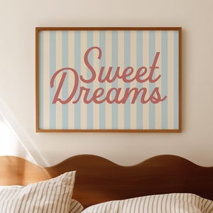 May include: A bedroom scene featuring a wooden headboard and striped bedding. A framed print with the words "Sweet Dreams" in a cursive font hangs above the bed. The print has a light blue and cream striped background.