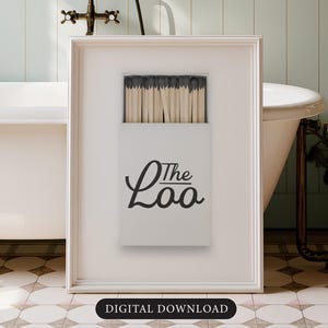 May include: A framed print featuring a white matchbox design with the text "The Loo" in black script. The match heads are black. The background includes a white bathtub, floral wallpaper, and a vintage faucet.