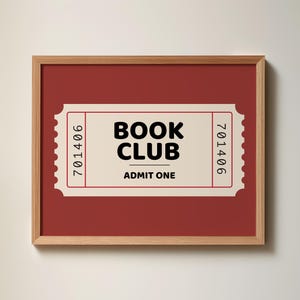May include: A framed print featuring a red background with a cream-colored ticket design. The ticket reads "BOOK CLUB" in bold black letters, with "ADMIT ONE" below. The frame is made of light brown wood.