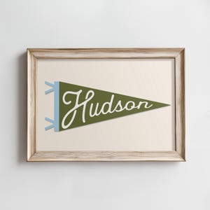 May include: A framed print of a green pennant with the word "Hudson" written in white cursive.