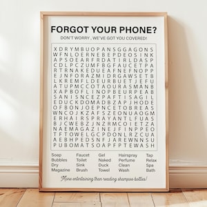 May include: A black and white printable word search puzzle with the words "Forgot your phone? Don't worry, we've got you covered!" at the top. The puzzle includes words related to bathroom items, such as soap, bubbles, faucet, toilet, gel, naked, hairspray, perfume, tap, relax, dry, sink, duck, clean, spa, magazine, brush, towel, and wash. The puzzle is framed in a light wood frame.