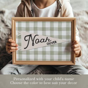 May include: A framed, personalized pennant with the name "Noah" in black script and "Oliver" in smaller black text. The pennant is cream-colored and set against a green and white gingham background. The frame is light brown.