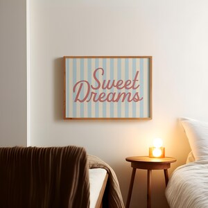 May include: A framed wall art piece with the words "Sweet Dreams" in a cursive font. The background has vertical stripes in light blue and off-white. The frame is made of wood.