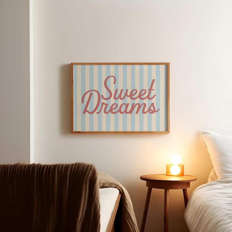 May include: A framed wall art piece with the words "Sweet Dreams" in a cursive font. The background has vertical stripes in light blue and off-white. The frame is made of wood.