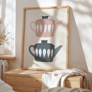 May include: A framed print with a minimalist design featuring two teapots. The top teapot is pink with white leaf-like patterns and the bottom teapot is gray with white leaf-like patterns.