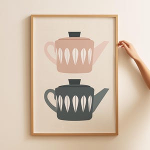 May include: A framed print of two teapots, one pink and one gray, with white leaf designs. The teapots are stacked on top of each other.