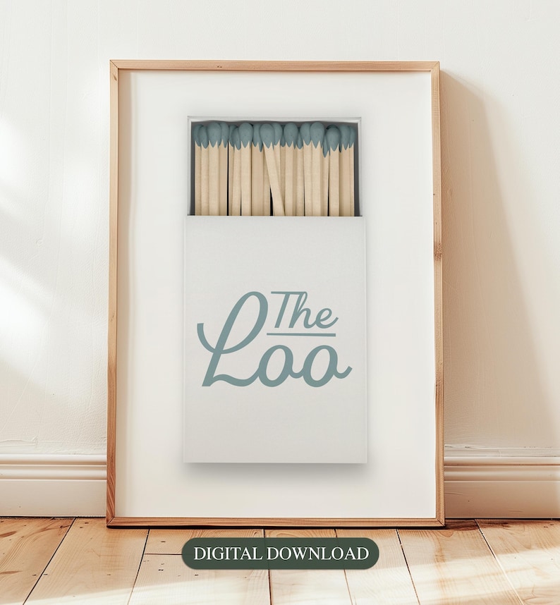 May include: A framed print of a white box with a blue and white design. The box contains a full pack of matches with blue tips. The text on the box reads "The Loo".
