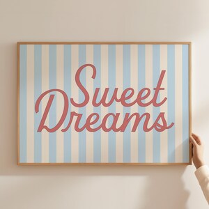 May include: A framed print with a light blue and white striped background. The words "Sweet Dreams" are written in a cursive, coral-colored font. The frame is made of light-colored wood.