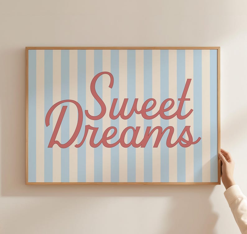 May include: A framed print with a light blue and white striped background. The words "Sweet Dreams" are written in a cursive, coral-colored font. The frame is made of light-colored wood.