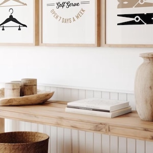May include: Three framed prints with laundry-themed designs. The first print features three white clothespins on a black background. The second print features a white logo with the text "The Davis Family Laundry Co. Self Serve Open 7 Days a Week". The third print features three brown clothespins on a white background.