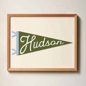 May include: A framed print of a green pennant with the word "Hudson" written in white script. The pennant has blue tassels.