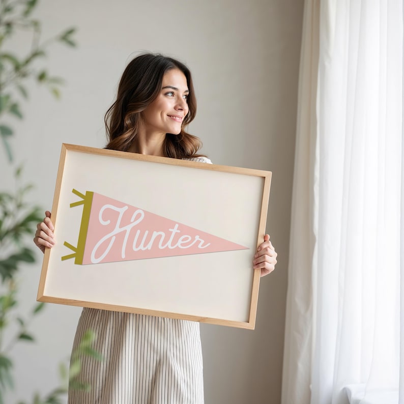 May include: A framed pink and white pennant with the word "Hunter" in white script. The pennant is in a wooden frame.