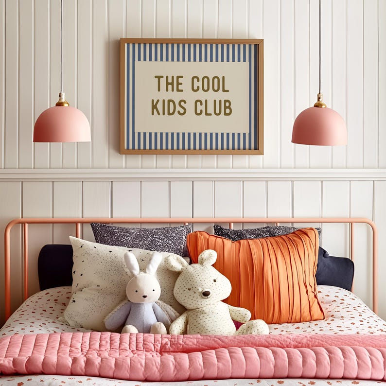 May include: A bedroom scene featuring a bed with a pink metal frame, adorned with pillows, stuffed animals, and a pink quilted blanket. Above the bed, a framed sign reads "THE COOL KIDS CLUB." Two pink pendant lights hang from the ceiling.