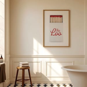 May include: A framed wall art print featuring a white matchbox with red-tipped matches and the red text The Loo printed on the front. The artwork is displayed in a thin wooden frame, showcasing a graphic design of a matchbox against a plain background.
