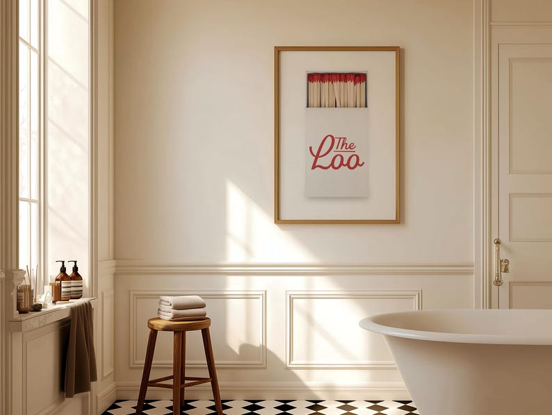 May include: A framed wall art print featuring a white matchbox with red-tipped matches and the red text The Loo printed on the front. The artwork is displayed in a thin wooden frame, showcasing a graphic design of a matchbox against a plain background.