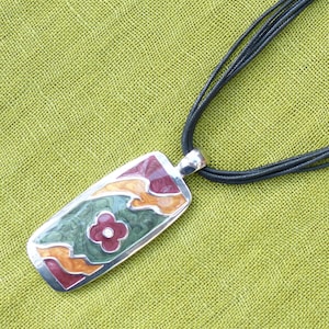 May include: A black multi-strand necklace with a rectangular pendant featuring a colourful abstract design with a flower in the centre.