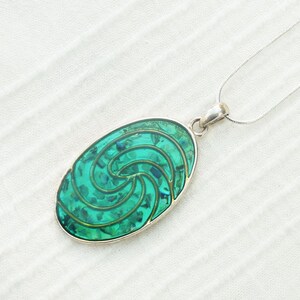 Può includere: Una collana con catena d'argento con un ciondolo ovale verde con un motivo a spirale.