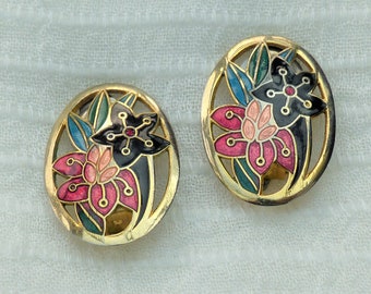 Puede incluir: Un par de pendientes de tono dorado con un diseño floral. Las flores son de color rosa, negro y azul con hojas verdes.