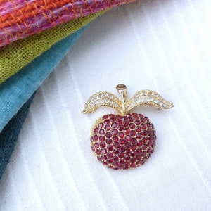 May include: A gold-tone brooch in the shape of an apple. The apple is covered in red rhinestones and the leaves are covered in clear rhinestones.