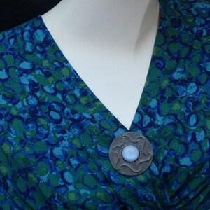 May include: A blue and green patterned fabric with a silver brooch featuring a blue stone in the center.
