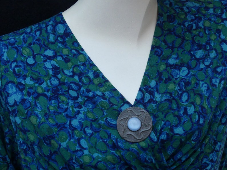 May include: A blue and green patterned fabric with a silver brooch featuring a blue stone in the center.