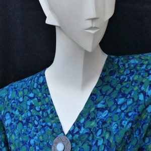May include: A blue and green patterned blouse with a silver and blue brooch. The brooch has a round, blue stone in the center.