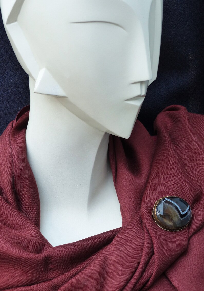 May include: A maroon scarf with a brown and white agate brooch. The brooch is oval shaped and has a silver setting.