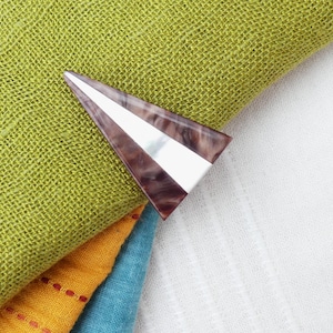 Può includere: Un fermaglio per capelli a forma triangolare con un design marmoreo marrone e bianco. Il fermaglio ha un accento in metallo argentato.