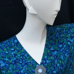 May include: A blue and green patterned dress with a silver and blue brooch.