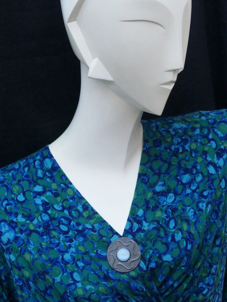 May include: A blue and green patterned dress with a silver and blue brooch.
