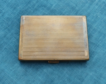 Könnte beinhalten: Ein goldfarbenes Metall-Etui mit geripptem Design. Das Etui hat einen Klappdeckel und einen kleinen Verschluss.