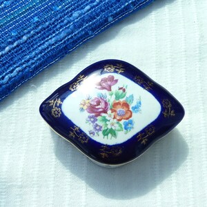 May include: A small, blue and white porcelain trinket box with a floral design. The box is shaped like a diamond and has a gold trim.