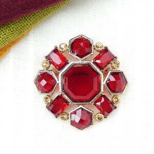 May include: A red jeweled brooch with a gold setting. The brooch is made up of eight red jewels, each with a different shape and size. The brooch is set on a white background.