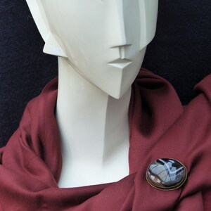 May include: A white mannequin wearing a maroon scarf with a round, black and white agate brooch.