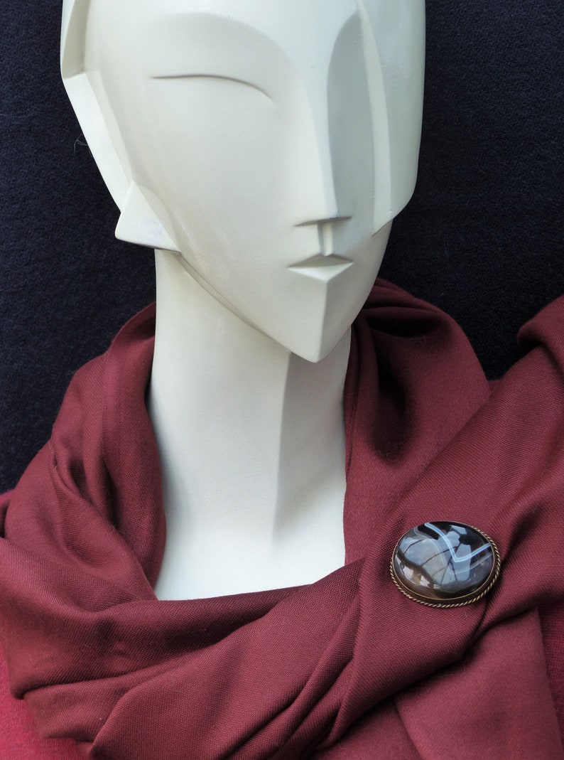 May include: A white mannequin wearing a maroon scarf with a round, black and white agate brooch.
