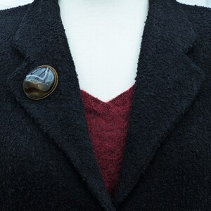 May include: A black blazer with a burgundy undershirt and a brown agate brooch with a silver setting.