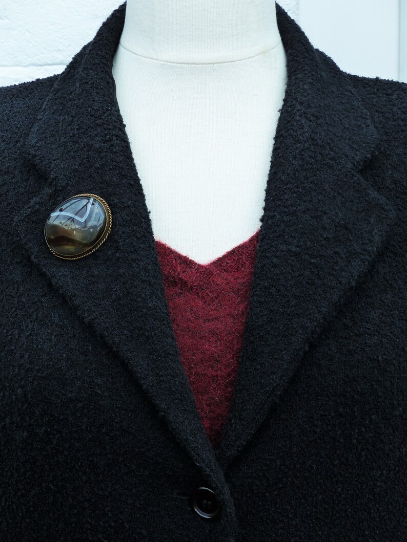 May include: A black blazer with a burgundy undershirt and a brown agate brooch with a silver setting.