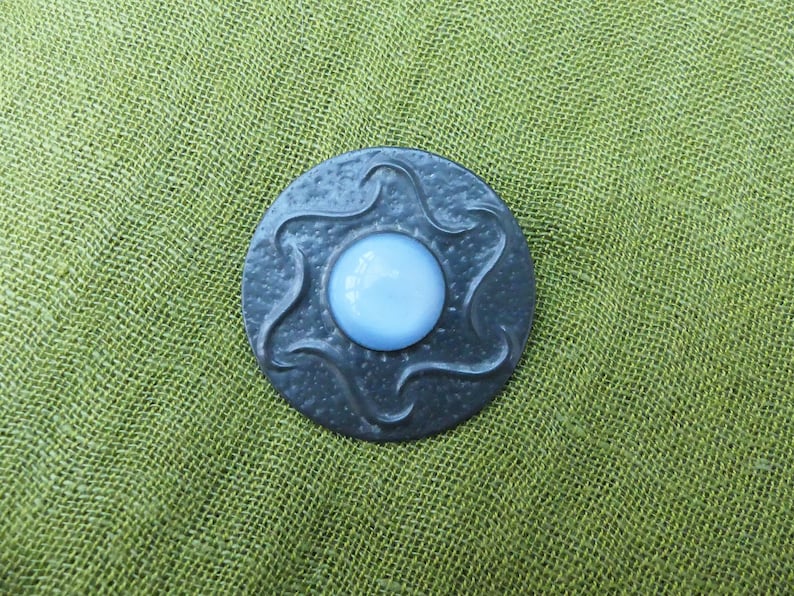 May include: A round, silver-colored brooch with a swirling design and a light blue glass center.