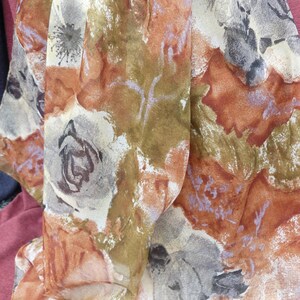 May include: A sheer scarf with a floral print in shades of brown, orange, and gray. The scarf is made of a lightweight fabric and has a delicate, flowing feel.