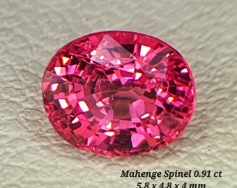 Puede incluir: Una piedra preciosa de espinela de Mahenge de color rosa vibrante, corte ovalado, con superficies facetadas que reflejan la luz. La piedra está etiquetada como Mahenge Spinel 0.91 ct, mide 5,8 x 4,8 x 4 mm y muestra un color brillante y saturado.