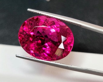 May include: A vibrant pink oval-shaped gemstone with facets, held by tweezers.