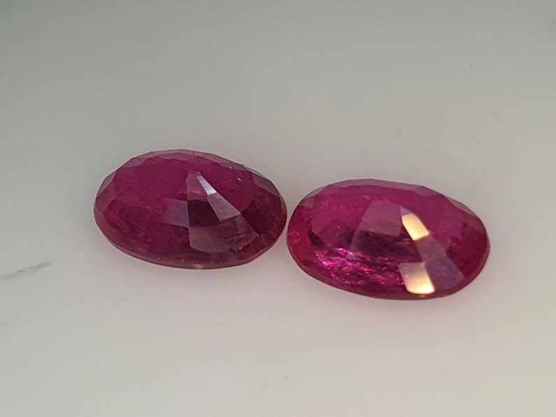 Op de afbeelding: Twee ovale, gefacetteerde robijn edelstenen. De robijnen zijn diep roze van kleur en hebben een hoge mate van glans.
